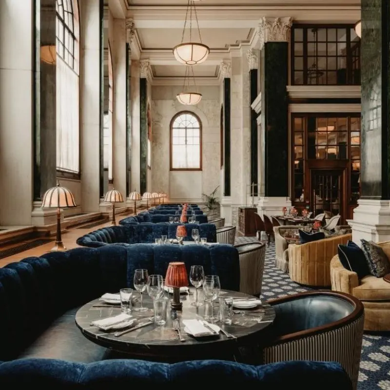 Dining room at The Ned London with marble columns and blue velvet banquettes