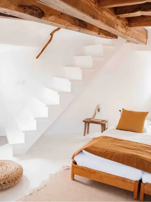 Whitewashed bedroom with exposed beams and sculptural staircase