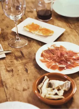 Table setting with wine, cured ham, bread, and small shared plates